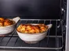 Two ceramic bowls filled with food are on an oven rack inside an oven. Produktbild-Vorschau