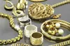 A collection of gold and silver jewelry, including necklaces, rings, earrings, and a bracelet, is displayed on a reflective gray surface. Produktbild-Vorschau