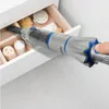 A hand holds a silver and blue handheld vacuum cleaner with a star-shaped grip, inserting its nozzle into an open drawer containing bathroom accessories. Náhled obrázku produktu