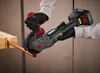 A person wearing black gloves is using a cordless angle grinder to cut a copper pipe. The pipe is held in place by a wooden clamp. The angle grinder has a battery attached. Produktbild-Vorschau