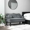 A dark gray velvet bench with tufted detailing and decorative studs is placed in a bedroom setting next to a bed. A large round mirror hangs on the wall above the bench, and a potted plant is visible to the left. Náhled obrázku produktu