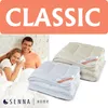 A couple is shown in bed, smiling and holding pillows, with two folded duvets in the foreground and midground. The text 'CLASSIC' is prominently displayed at the top. Voir les images du produit