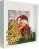 A festive shadow box frame with a baby dressed as Santa Claus, a miniature Christmas tree, and gift decorations. Náhled obrázku produktu