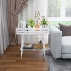 A white wooden plant stand with books and plants on it, placed next to a gray sofa in a living room. Produktbild-Vorschau