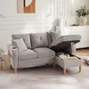 A light gray sectional sofa with its storage ottoman open, revealing stored items. The sofa is in a well-lit living room with decorative elements on the wall and a dresser in the background. Náhľad obrázku produktu