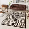 A living room scene with a brown leather sofa, a zebra-patterned rug, and wooden furniture. Produktbild-Vorschau