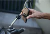 A hand is holding a smartphone with a mount attached to it, near a motorcycle mirror. Náhled obrázku produktu