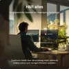 A person is working at a desk with two monitors, one labeled 'DESKTRONIC' with a checkmark and the other labeled 'ANDERE' with an 'X'. The scene is set in a well-lit office with a window in the background. Produktbild-Vorschau