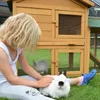 A young girl petting a white rabbit in front of a wooden rabbit hutch. Produktbild-Vorschau