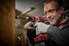 A man is using a red and gray cordless drill to drill into a wooden beam. Wood chips are flying from the beam. Produktbild-Vorschau