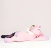 A young girl is lying on a large pink plush unicorn. Voir les images du produit