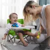 Lächelndes Baby in einem limettengrünen tragbaren Hochstuhl mit weißem Tablett, spielt mit einem blauen Spielzeugauto, während eine Frau sie anlächelt Náhled obrázku produktu
