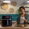 A woman is in a kitchen, looking at a steak on a plate next to an air fryer. Anteprima dell’immagine prodotto