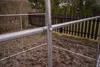 Close-up of a metal frame structure, likely for a greenhouse or tunnel, with a wooden fence and trees in the background. Náhľad obrázku produktu