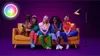 Four people and a dog sitting on a couch in front of a purple background, with a floor lamp and a colorful logo in the corner. Voir les images du produit