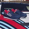 A pair of blue and red Sparco Martini Racing sneakers are placed on the hood of a car with Martini racing stripes. Produktbild-Vorschau