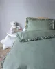 A close-up view of a baby bed with mint green bedding and a teddy bear on a side table. Anteprima dell’immagine prodotto