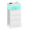 A white nightstand with three drawers and an open compartment illuminated by blue LED lights. The top surface displays a smartphone, headphones, a book, a charging cable, and a cup on a saucer. Produktbild-Vorschau