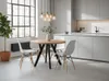 A modern dining room with a round wooden table and four white chairs, set against a backdrop of a large window and a sleek kitchen. Produktbild-Vorschau