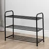 A black metal shoe rack with three shelves, shown in a room with a wooden floor and a light-colored wall. Náhľad obrázku produktu