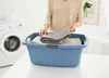 A person is folding laundry into a blue laundry basket next to a washing machine. Náhled obrázku produktu