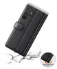 A black leather flip case for a smartphone is shown at an angle, appearing to be dropped onto a cracked surface, illustrating its protective qualities. Produktbild-Vorschau