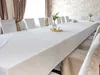 A long white tablecloth is laid out on a table, set with chairs covered in white slipcovers, in a room with neutral-toned curtains and patterned wallpaper. Produktbild-Vorschau