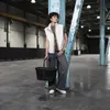 A person stands in a large, industrial-looking space, holding a black basket. Voir les images du produit