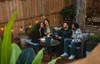 Four people are sitting on a patio, laughing and talking around a small fire pit. Produktbild-Vorschau