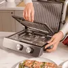 A person is using an electric grill in a kitchen setting, with food on a plate in the foreground. Voir les images du produit