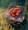 A piece of seasoned meat is being grilled on a small portable grill outdoors. Podgląd zdjęcia produktu
