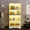 A modern, illuminated glass display cabinet filled with books, decorative items, and bottles. Náhled obrázku produktu