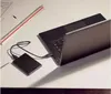 A black external hard drive is connected to a black laptop on a white desk. A ruler is visible in the background. Produktbild-Vorschau