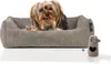 A small dog is lying in a dog bed next to a poop bag dispenser. Produktbild-Vorschau