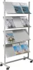 A white metal magazine rack with multiple shelves, each holding magazines. The rack is on wheels. Anteprima dell’immagine prodotto
