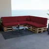 A sectional sofa made of wooden pallets with dark red cushions is placed on a balcony overlooking the ocean. Voir les images du produit