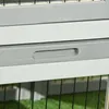 A close-up view of a grey and white wooden structure, possibly part of a pet enclosure, with a black wire mesh visible at the bottom. Podgląd zdjęcia produktu