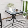 A small square glass-top table with a black metal frame is set up on an outdoor patio or balcony, decorated with a vase of flowers, a cup of coffee, and a candle. Podgląd zdjęcia produktu
