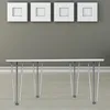 A white table with silver hairpin legs is shown in front of a gray wall with four white square picture frames above it. Anteprima dell’immagine prodotto