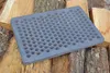 A cast iron grate with many circular holes rests on a pile of firewood. Náhled obrázku produktu