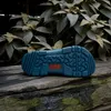The sole of a blue Birkenstock Super Birki clog is shown resting on a weathered wooden surface, with lush green foliage in the background. Produktbild-Vorschau