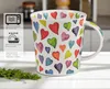 A white mug with colorful heart patterns is shown on a table with some greenery in the foreground. To the left of the mug, there is a panel with icons and text indicating product features. Produktbild-Vorschau