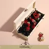 An open wooden box filled with chocolates, with one chocolate outside the box. Produktbild-Vorschau