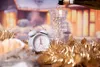 A festive scene with an alarm clock, a glass of champagne being poured, and gold tinsel, suggesting a New Year's celebration. Anteprima dell’immagine prodotto