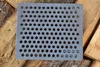 A gray cast iron grate with many holes is placed on a pile of logs. Voir les images du produit