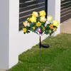 A solar-powered flower light stake is planted in a grassy lawn next to a white wall and a dark fence. Náhled obrázku produktu