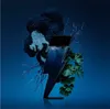 A lightning bolt-shaped perfume bottle is surrounded by dark, textured organic elements and green leaves against a deep blue background. Náhľad obrázku produktu