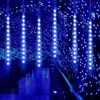 Blue meteor shower string lights hanging over a reflective surface, possibly water, with a bokeh background of blue and white lights. Produktbild-Vorschau