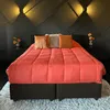 A bed with a coral-colored comforter and pillows in a modern bedroom setting. Produktbild-Vorschau