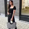 A woman stands on a sidewalk holding a shopping bag. Podgląd zdjęcia produktu